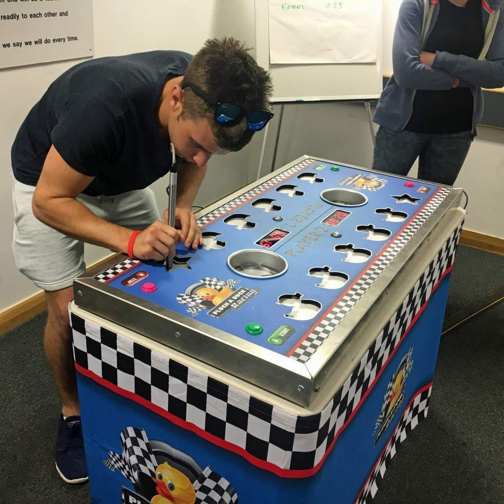 Adults seriously focusing on using the magnetic rod to pick up the metal ducks as a timer counts down at an indoor University event.