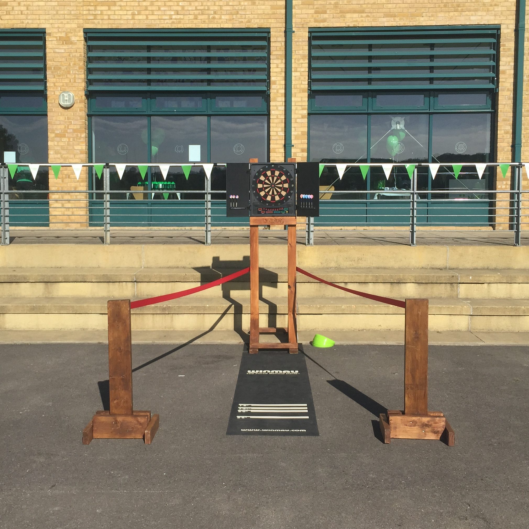Our Dartboard with our bespoke wooden frame, rubber dart mat, premium rope red rope barrier and bespoke hand-made barrier stands, all set out for play.