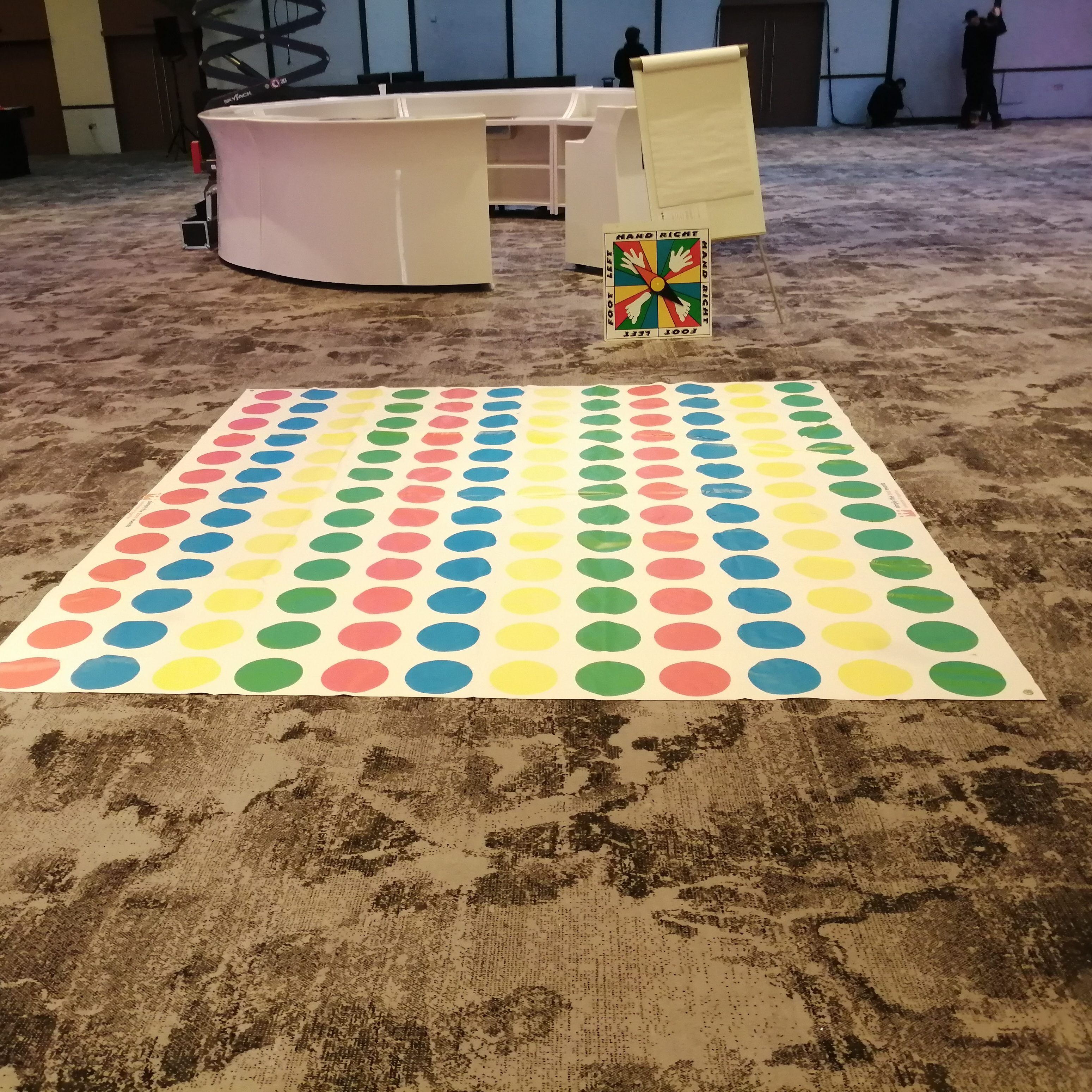 An empty Twister mat lying on a carpeted floor with the Twister board ready.