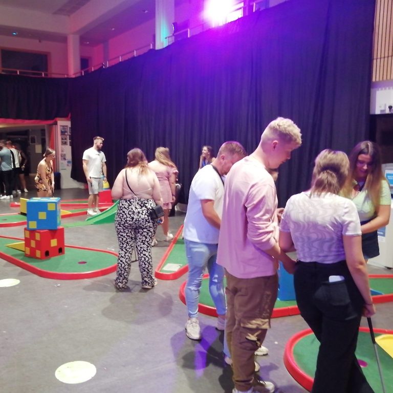Our popular Crazy Golf with a large group of students watching and playing in a University hall for a Freshers Fayre event.