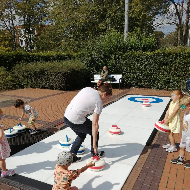 People playing Curling on a sunny day, at a Street event.
