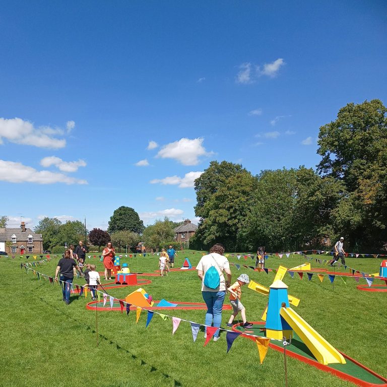 Crazy Golf and bright bunting hired for a fete event with lots of people playing or watching.