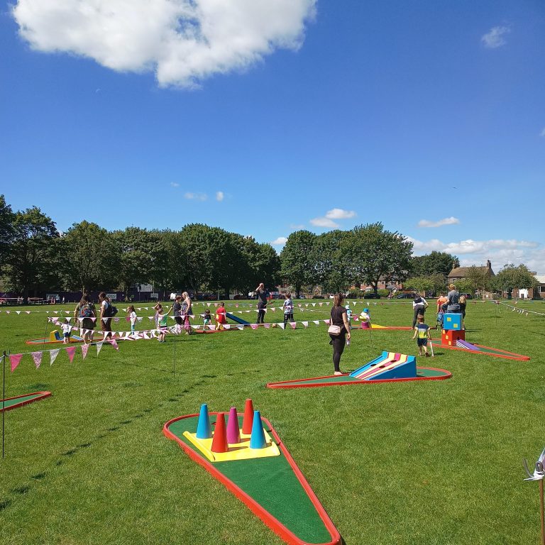 Our Crazy Golf with brightly painted obstacles set out on grass with lots of colourful bunting.