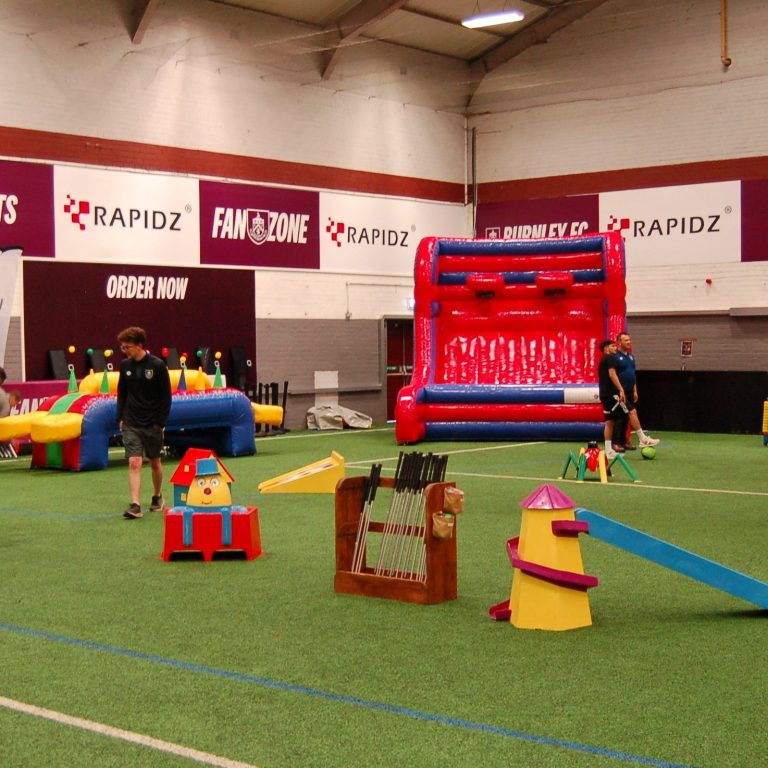 Crazy Golf hired and set up for an indoor event with our bespoke wooden holder for the golf clubs and golf balls and two Big Impact Inflatables in the background (Inflatable Hoverball and Inflatable Basketball).