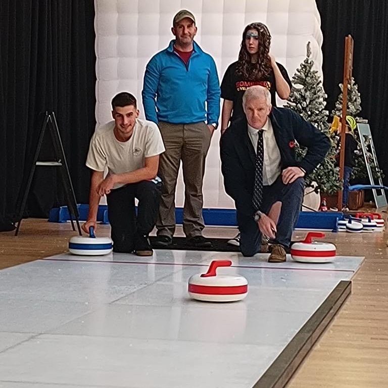 A group of adults with two bent down on one knee as they take turns to play Curling.