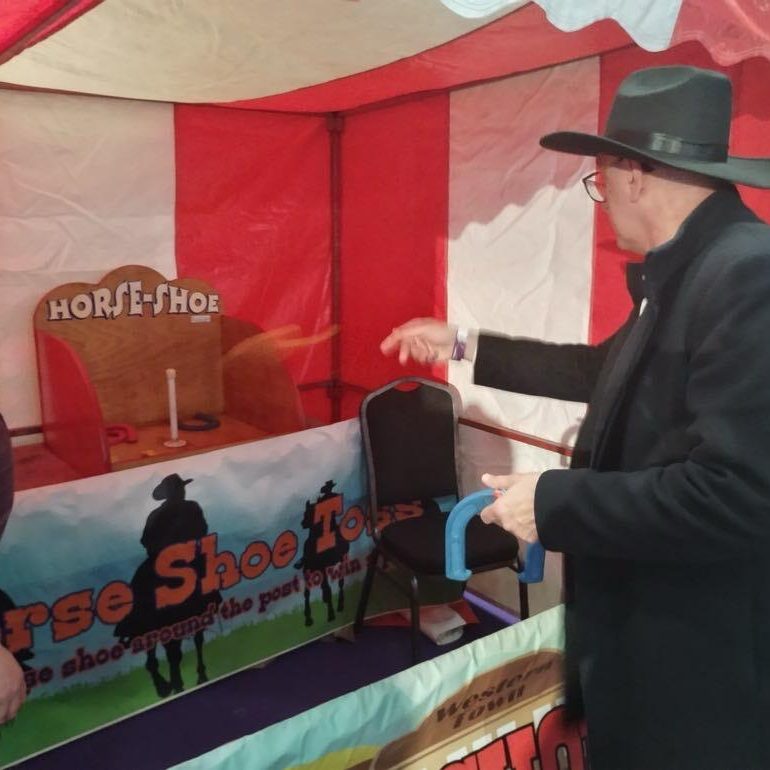 Adults at a Western themed office party throwing horseshoes at the target which is inside one of our hired Side Stalls.