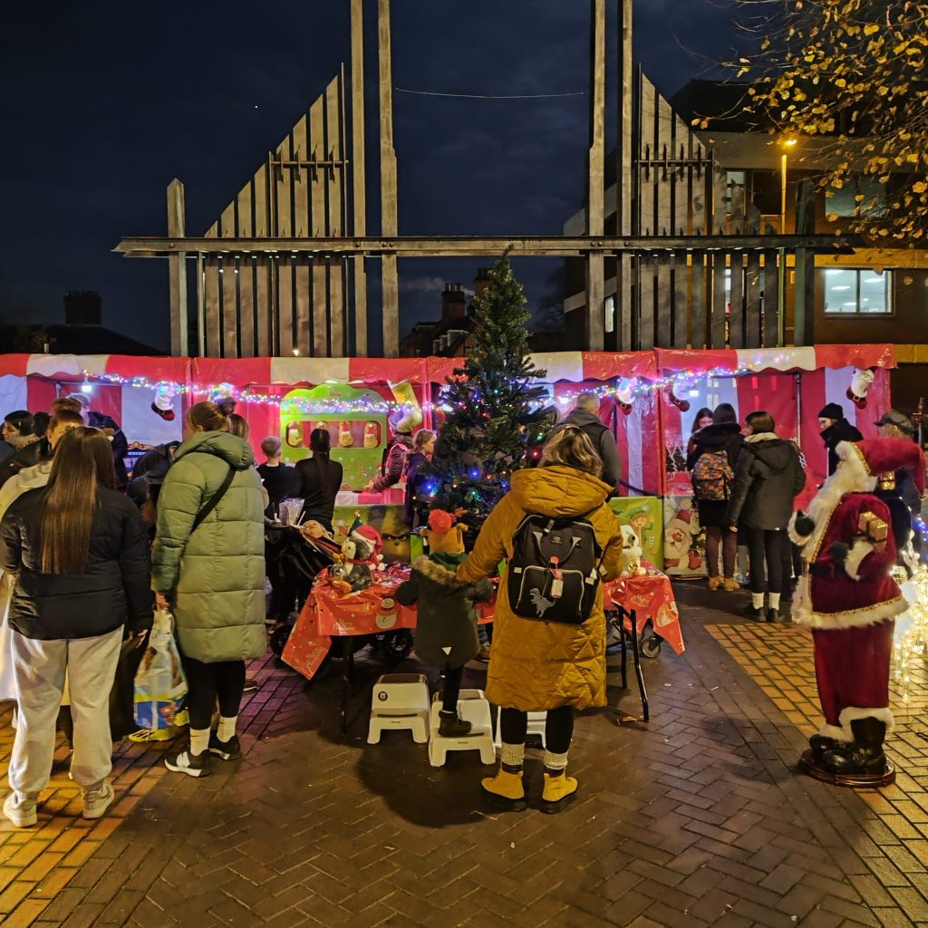 Our Festive Christmas Market Side Stalls in a row with our Christmas Tree and decorations being enjoyed by a group of families.