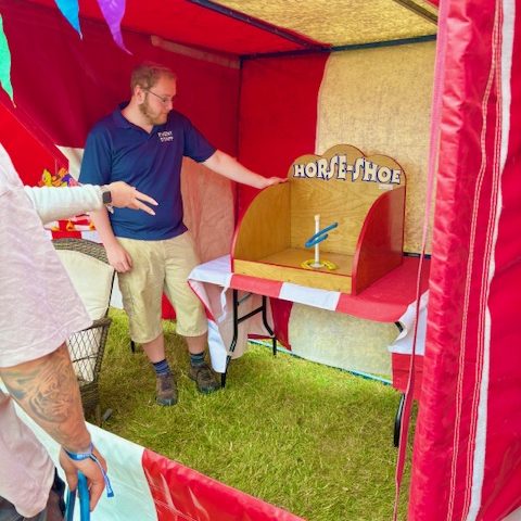 An action shot of our hired in red and white striped Down a Clown Side Stall showing a man's arm having just thrown a colourful plastic horseshoe.