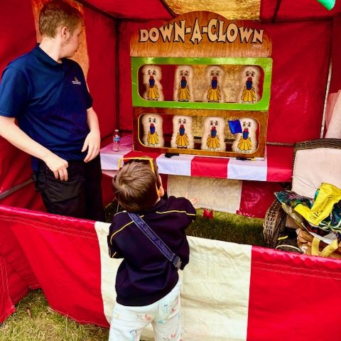Young boy playing on our hired in Down a Clown Side Stall, with a member of our staff watching and with the beanbag captured in mid air.