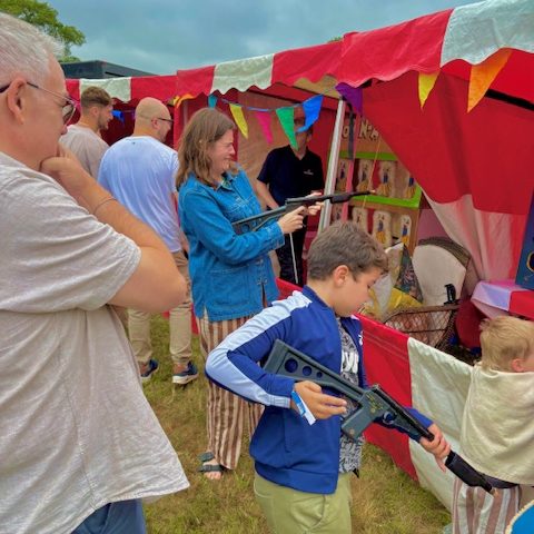 A woman and a young boy both having a go at using our cork shooting guns to shoot the target with the woman playfully grimacing and a man on the left watching intently.