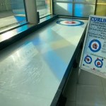 A Curling Lane set up in an office with an instruction A Frame sign next to it.
