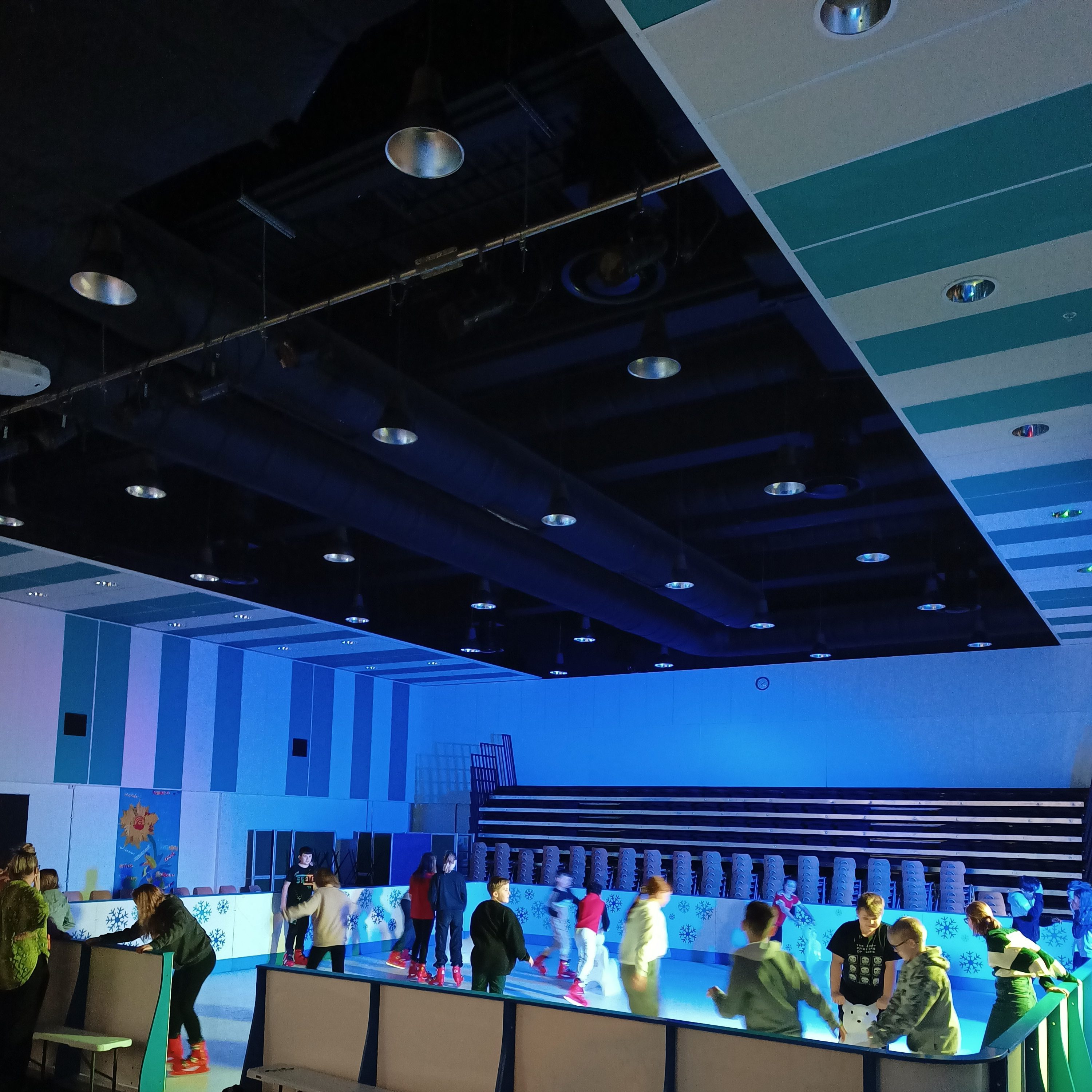 A shot of an indoor installed Ice Rink with a crowd of skaters.