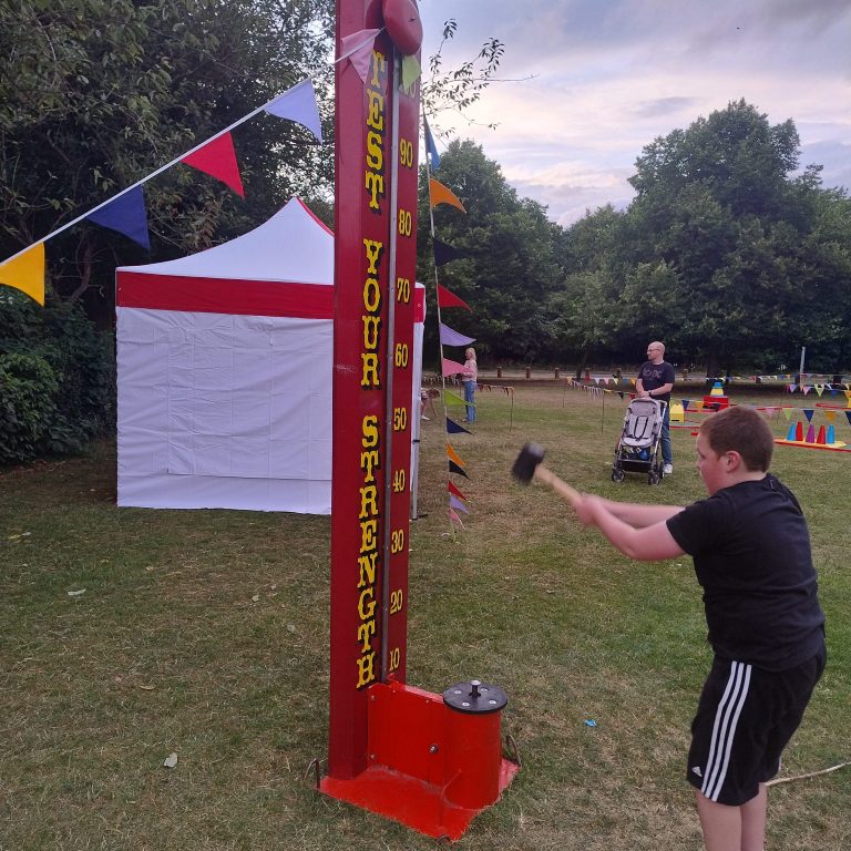 Our bright red and gold High Striker/ Test your Strength game with someone using a rubber mallet to hit it.