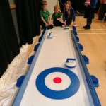 School children having a go at the Child Sized Curling Lane in a school gym for a fundraising event.