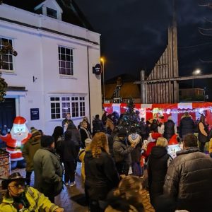 A crowded brick street with a row of bright red and white Christmas Carnival Side Stalls and lots of festive decorations at Christmas Market Event.