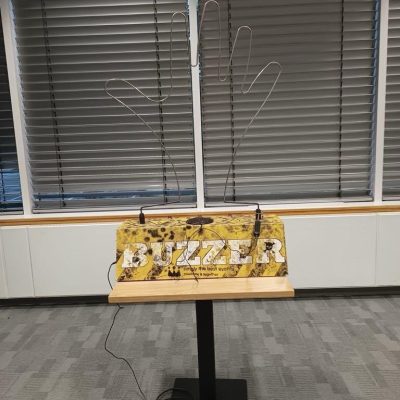 Our Giant Buzzer set up with its camouflage patterned base, metal tong and wire in the shape of a hand.