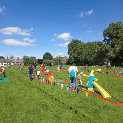Our Crazy Golf with brightly painted obstacles set out on grass with lots of colourful bunting.