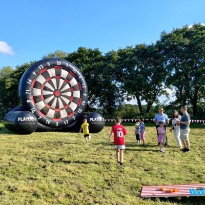 Our Giant Inflatable Dartboard set out on grass with children playing and trying to kick the football onto it for a score.