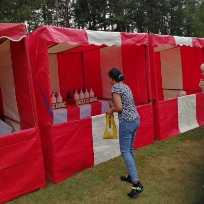 A woman at a Village Fete event, poised ready to throw a hoop at out Ring the Bottle Side Stall game, with more of our Side Stalls set up on either side.