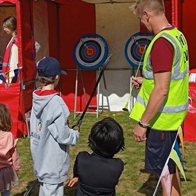 Children at a village fete playing soft archery, which is positioned inside one of our hired in Side Stalls, with bunting.