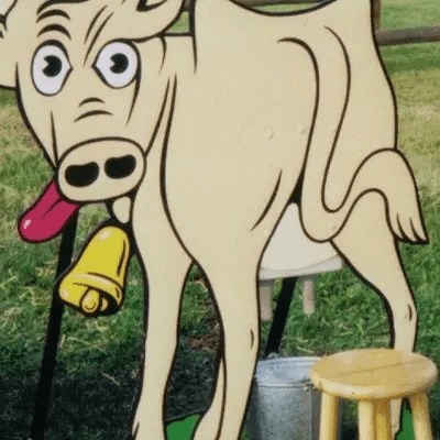 Gertrude, our cute cow with its tongue sticking out and a bell around its neck, propped up securely with a milking stool and bucket.