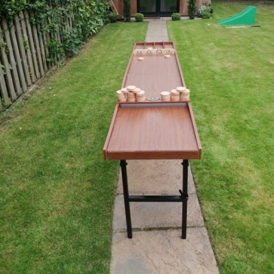 The wooden game of Sjoelbak set up with legs in a garden for a family garden party.